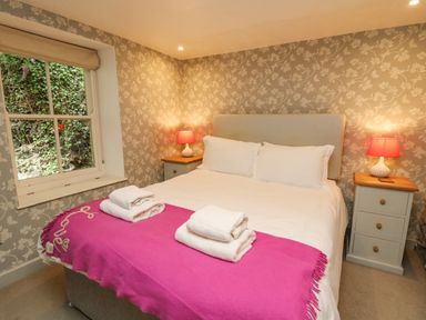 A bedroom with a bed covered with white linens and a pink blanket with towels on top and bedside tables with lamps at Tan y Craig in Solva