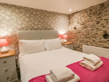 A bedroom with a bed with white bedding and towels on a pink blanket two bedside tables with lamps and a stone wall at Tan y Craig in Solva