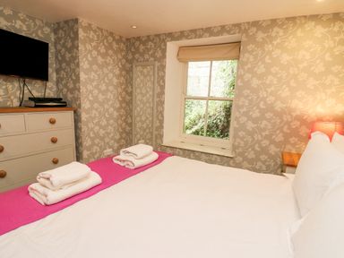 A bedroom with a bed folded towels a window a chest of drawers and a wall-mounted television at Tan y Craig in Solva