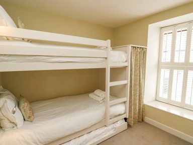 A bedroom with a white bunk bed near a window with shutters and patterned curtains at Tan y Craig in Solva