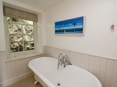 A bathroom with a clawfoot bathtub under a window and a painting on the wall at Tan y Craig in Solva