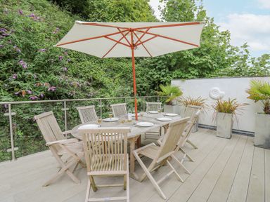 An outdoor wooden dining table with eight chairs and a large umbrella on a deck at Tan y Craig in Solva