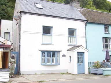 A white two story house with blue window frames and door next to a blue building with people sitting outside at Tan y Craig in Solva
