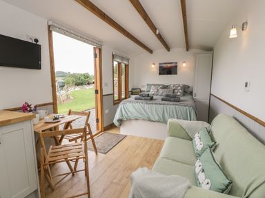 A bedroom with a bed green sofa wooden table and chairs open door showing outside at Tan Y Castell Shepherds Hut in Llangollen