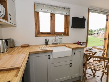 A kitchen with wooden countertops, a white sink, kettle, toaster, and a small dining table with chairs at Tan Y Castell Shepherds Hut in Llangollen