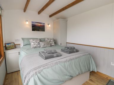 A bedroom with a bed covered in light green bedding and grey towels on top at Tan Y Castell Shepherds Hut in Llangollen