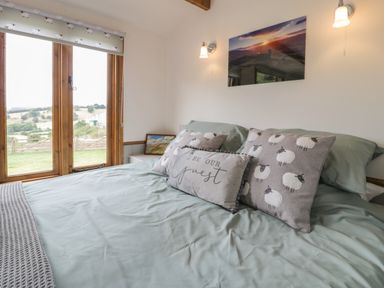 A bedroom with a bed with decorative pillows and large windows showing a countryside view at Tan Y Castell Shepherds Hut in Llangollen