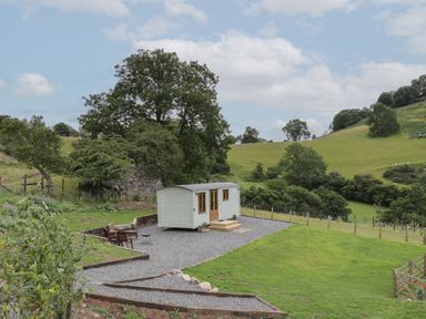 A small white shepherds hut on a gravel area with outdoor seating in a rural landscape at Tan Y Castell Shepherds Hut in Llangollen
