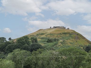 A hill with a winding path and ruins at the top surrounded by trees at Tan Y Castell Shepherds Hut in Llangollen