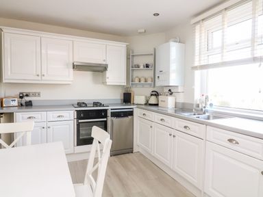 A kitchen with white cabinets a dining table and chairs a stove oven dishwasher and a window at 1 Camperdown Lodge in Salcombe