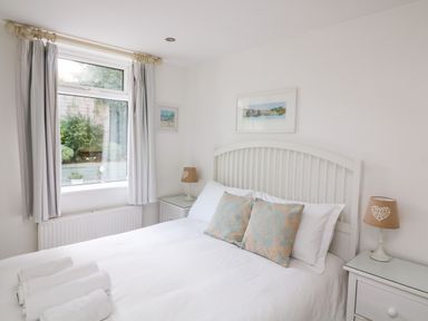 A bedroom with a double bed white bedding two pillows bedside tables with lamps and a window with curtains at 1 Camperdown Lodge in Salcombe