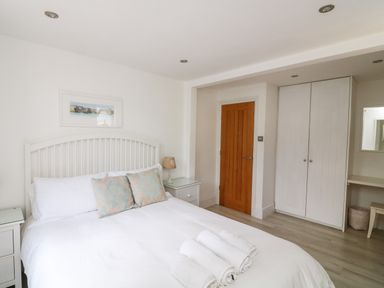A bedroom with a white bed and headboard beside wooden door and white wardrobe at 1 Camperdown Lodge in Salcombe