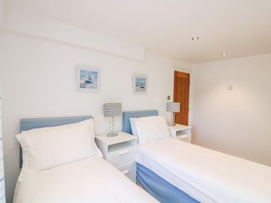 A bedroom with two single beds bedside tables lamps and framed pictures on the wall at 1 Camperdown Lodge in Salcombe