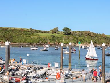 A marina with boats docked and people walking on the pier with a view of green hills in the background at 1 Camperdown Lodge in Salcombe