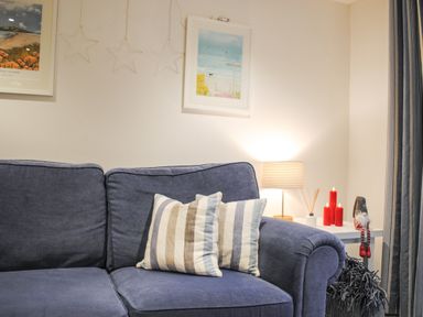 A blue sofa with striped cushions near a side table with a lamp red candles and a decorative figure at 1 Camperdown Lodge in Salcombe