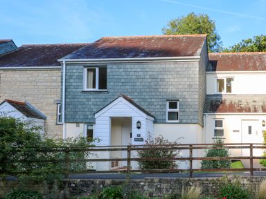 A two-story house with grey slate siding and a porch behind a wooden fence at Primrose Cottage in Goldenbank near Falmouth