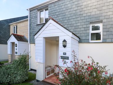 The entrance of a house with white porch and tiled floor with red flowers in the front at Primrose Cottage Goldenbank near Falmouth