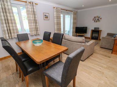 A dining area with a wooden table and six chairs next to a living room with sofas a television and a fireplace at Primrose Cottage Goldenbank near Falmouth