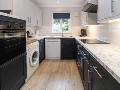 A kitchen with black and white cabinets a washing machine a dishwasher and a window at Primrose Cottage in Goldenbank near Falmouth