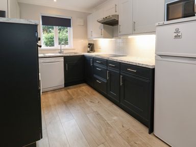 A kitchen with dark lower cabinets white upper cabinets a white refrigerator and dishwasher and a window with a blind at Primrose Cottage in Goldenbank near Falmouth