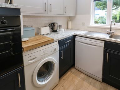 A kitchen corner with washing machine dishwasher sink kettle toaster and cabinets at Primrose Cottage Goldenbank near Falmouth