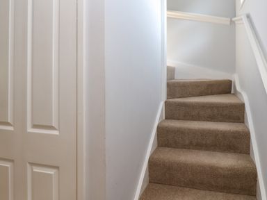 A staircase with beige carpet and white walls next to a closed white paneled door at Primrose Cottage in Goldenbank near Falmouth