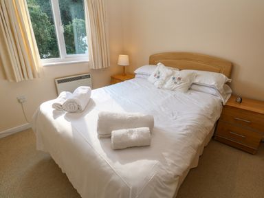 A bedroom with a double bed white linens rolled towels wooden bedside tables and a window at Primrose Cottage Goldenbank near Falmouth