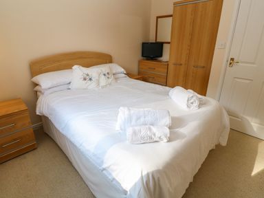 A bedroom with a double bed with white bedding and towels a wooden wardrobe wooden drawers and a small television at Primrose Cottage Goldenbank near Falmouth
