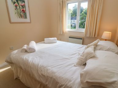 A bedroom with a double bed white linens rolled towels a window and a lamp at Primrose Cottage Goldenbank near Falmouth