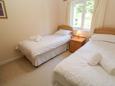 A bedroom with two single beds a nightstand with a lamp and a window at Primrose Cottage in Goldenbank near Falmouth