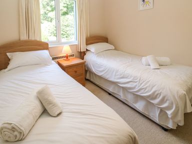 A bedroom with two single beds, a wooden nightstand with a lamp, and rolled towels on the beds at Primrose Cottage in Goldenbank near Falmouth