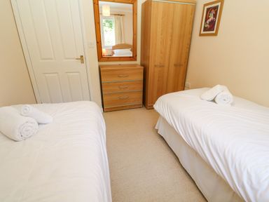A bedroom with two single beds with white linens and towels a wooden chest of drawers and wardrobe with a mirror on the wall at Primrose Cottage Goldenbank near Falmouth