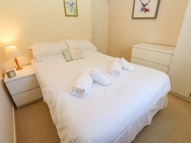 A bedroom with a double bed white bedding rolled towels bedside table with lamp and clock chest of drawers at Primrose Cottage Goldenbank near Falmouth
