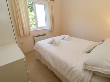 A bedroom with a double bed with white bedding and towels on the bed next to a window with cream curtains at Primrose Cottage in Goldenbank near Falmouth