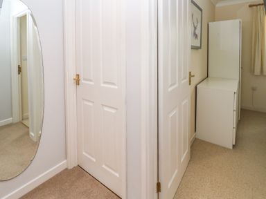 A hallway with two white doors a tall mirror on one wall and white cabinets in a carpeted room at Primrose Cottage Goldenbank near Falmouth