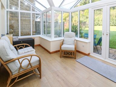 A conservatory with two cushioned chairs and glass walls overlooking a garden at Primrose Cottage Goldenbank near Falmouth