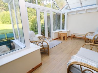 A conservatory with wooden floor cushions a sofa and armchairs at Primrose Cottage Goldenbank near Falmouth