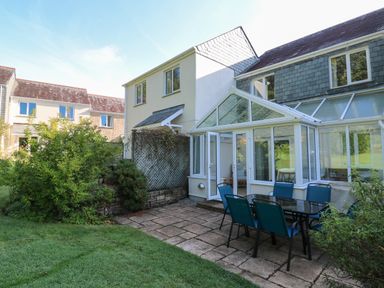 A patio area with a glass dining table and six chairs outside a house with a conservatory at Primrose Cottage Goldenbank near Falmouth