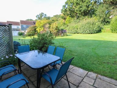 A garden patio with a glass table and blue chairs overlooking a green lawn and bushes at Primrose Cottage Goldenbank near Falmouth