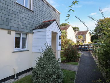The front entrance of a house with a small porch and garden next to a paved pathway and other houses in the background at Primrose Cottage in Goldenbank near Falmouth