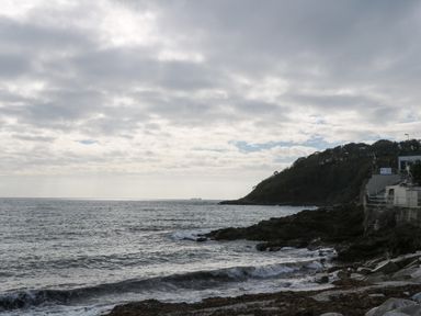 A rocky coastline with waves and a hill with trees near a concrete structure at Primrose Cottage in Goldenbank near Falmouth