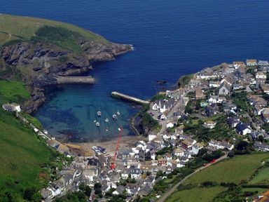 An aerial view of a coastal village with houses boats in a small harbor and green hills at St Samson in Port Isaac