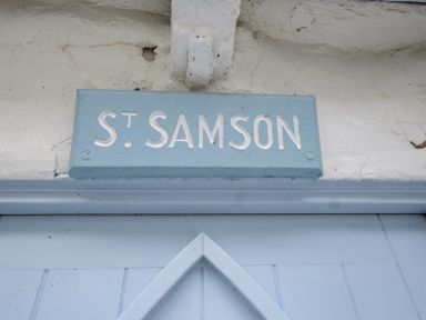 A blue sign with white text reading St Samson mounted above a light blue door at St Samson in Port Isaac