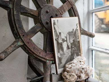 A ship wheel with an old black and white photograph and stones on a windowsill at St Samson Port Isaac