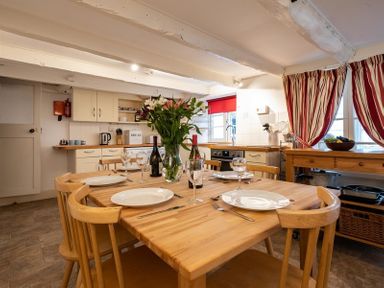 A kitchen with a wooden dining table set for four with plates glasses and wine bottles at St Samson in Port Isaac