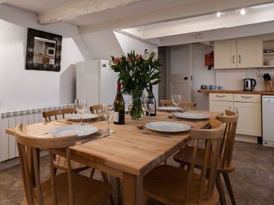 A dining room with a wooden table set for six with plates wine glasses and flowers at St Samson in Port Isaac