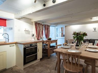 A kitchen with a wooden dining table set with plates glasses and a vase of flowers at St Samson in Port Isaac