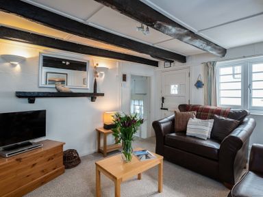 A living room with a leather sofa a wooden coffee table with flowers a wooden chest under a wall mirror and exposed ceiling beams at St Samson in Port Isaac