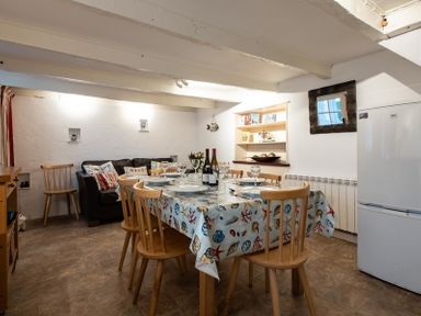 A dining area with a table set with plates and wine glasses surrounded by wooden chairs and a small black sofa at St Samson in Port Isaac