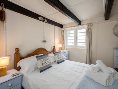A bedroom with a wooden bed frame two pillows bedside tables with lamps and rolled towels on the bed at St Samson in Port Isaac